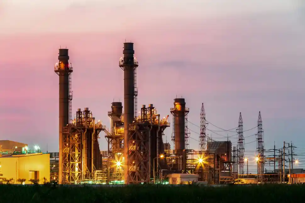 Power plant with illuminated towers against a dusk sky, showcasing industrial strength.
