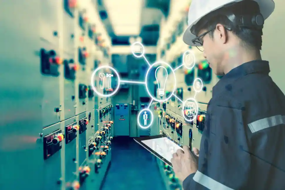 Engineer in hard hat using a tablet to manage control panels in a high-tech industrial facility.