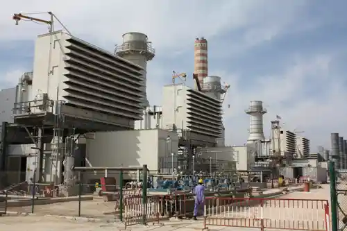 Industrial energy facility with multiple cooling towers and piping systems under a clear sky.