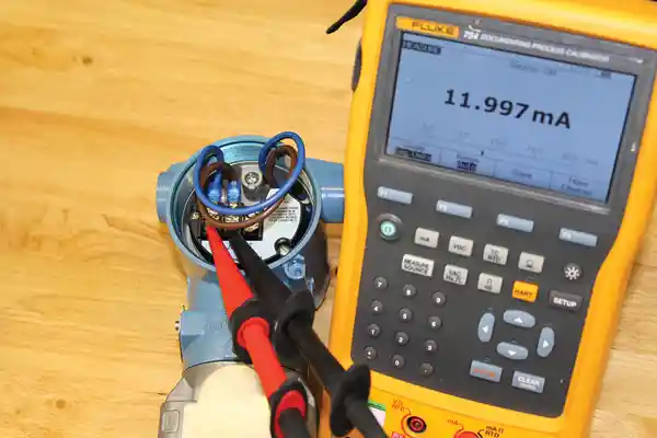 Multimeter measuring device displaying current reading alongside equipment on a wooden surface.
