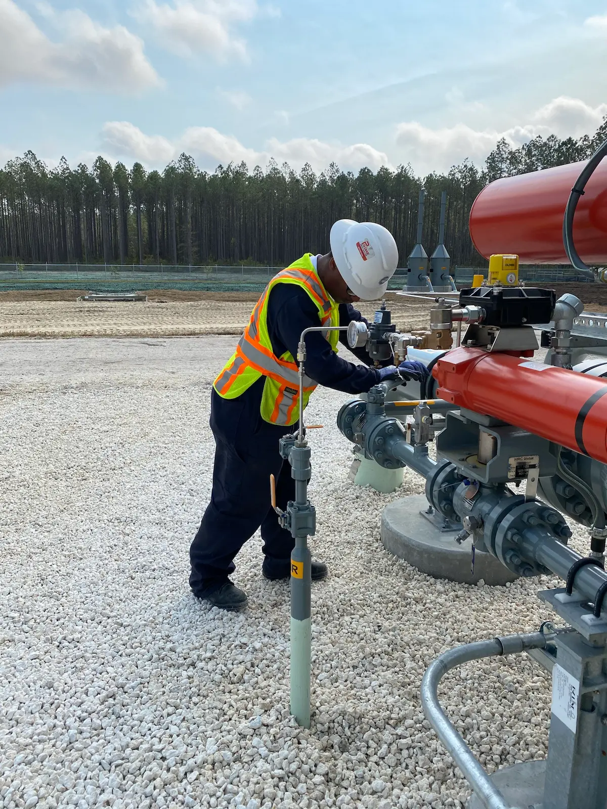Industrial worker in safety gear performing maintenance on gas pipeline equipment outdoors.