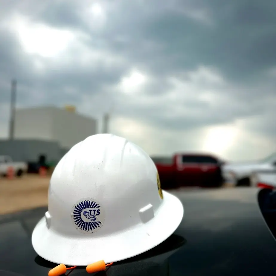 White hard hat with TTS logo in an industrial setting, highlighting safety in industrial services.