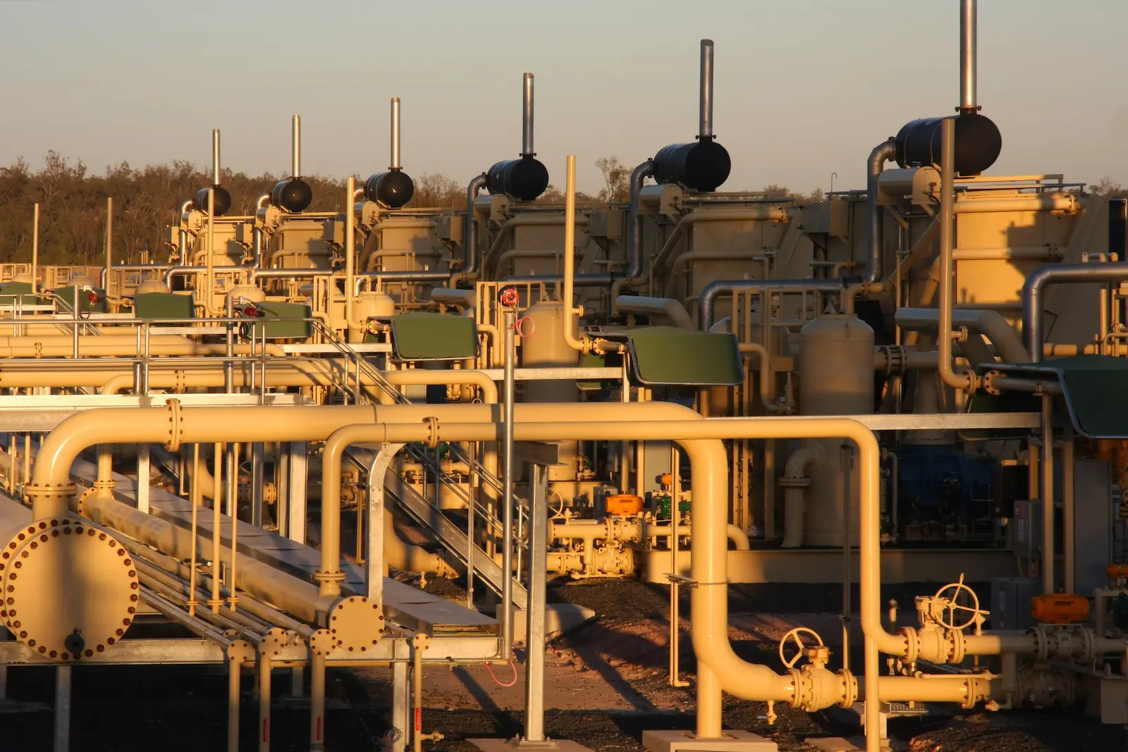 Industrial site with extensive piping and machinery, highlighted by the warm light of dawn or dusk, representing the complexity and scale of industrial services.