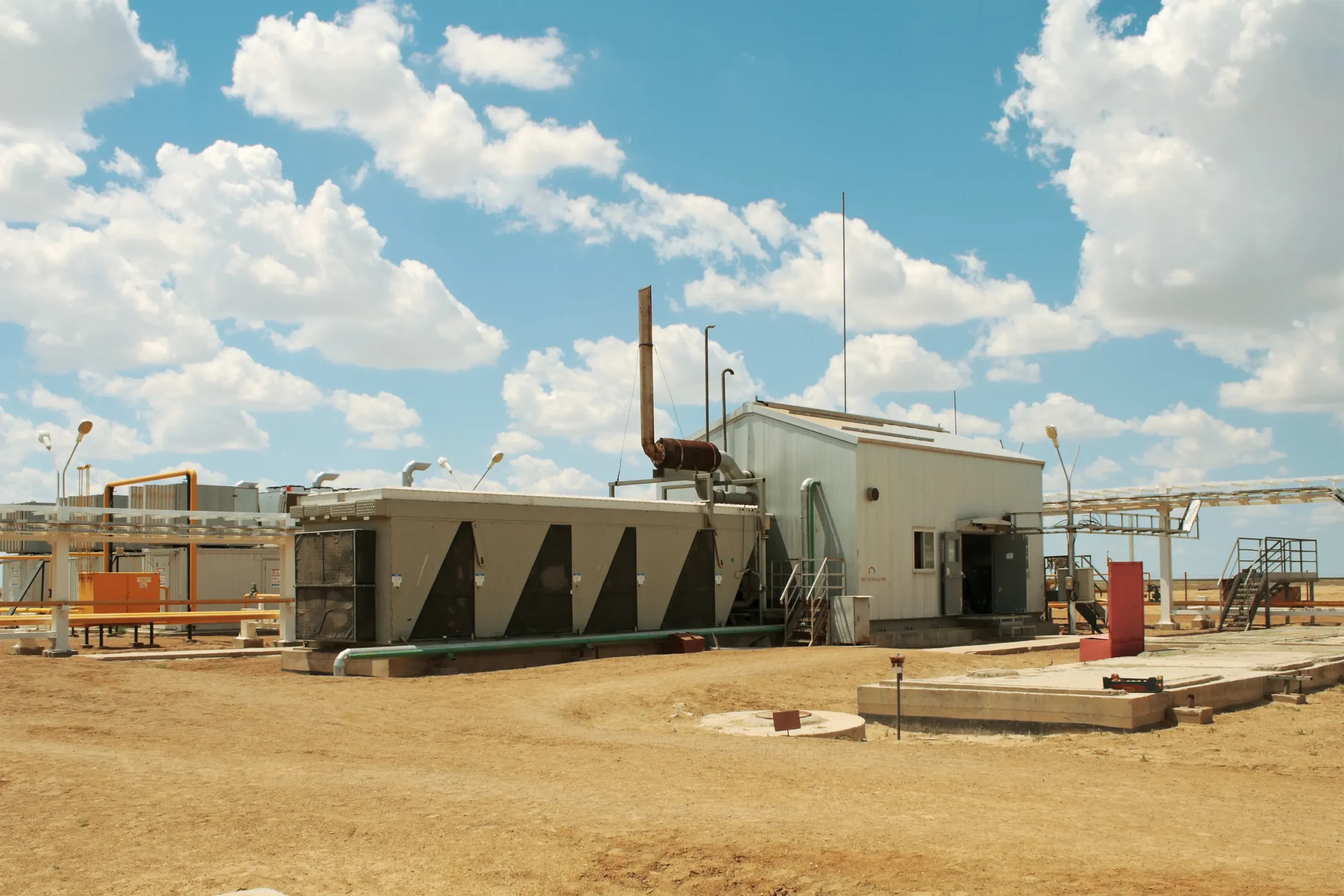 Industrial facility in a dry landscape with blue skies, showcasing infrastructure related to energy or manufacturing services.