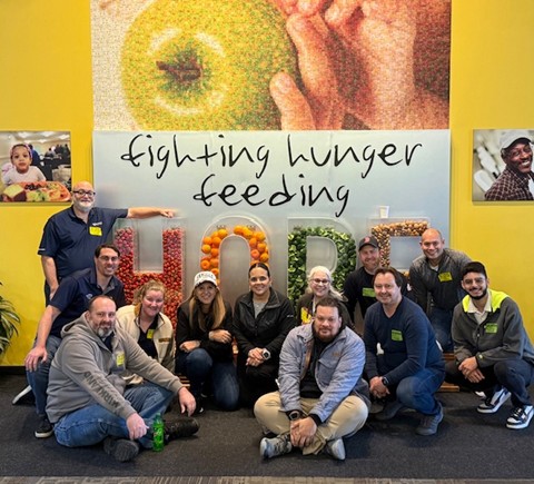 Group of people posing in front of a colorful display that reads 'fighting hunger feeding hope'.